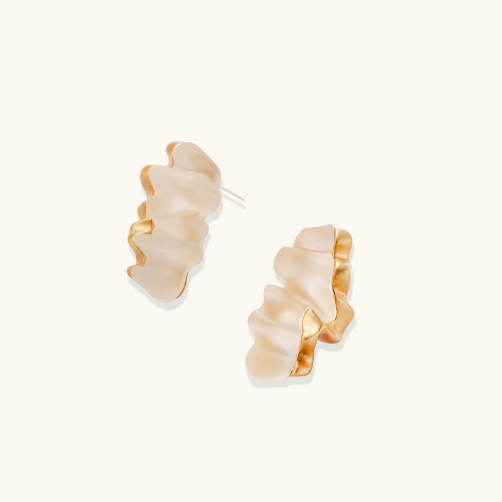 Sculptural gold-edged earrings with translucent resin centers in flowing wave shapes on neutral background.