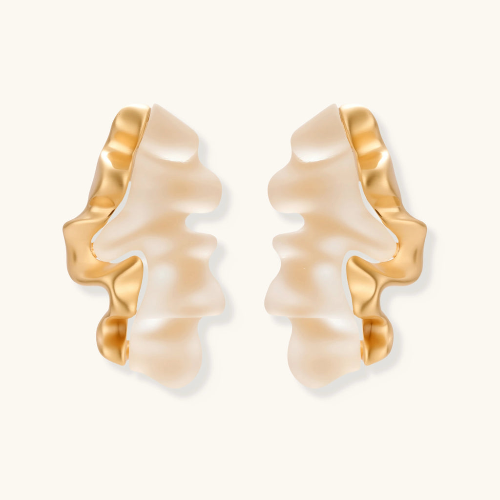 Sculptural gold-edged earrings with translucent resin centers in flowing wave shapes on neutral background.
