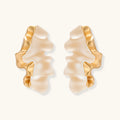 Sculptural gold-edged earrings with translucent resin centers in flowing wave shapes on neutral background.