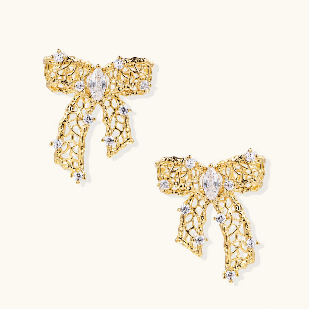 Gold-plated bow earrings with openwork design, marquise center stones, and flowing ribbon tails adorned with zirconia crystals.