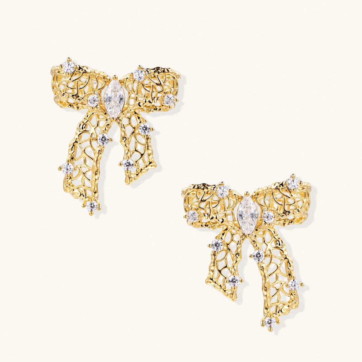 Gold-plated bow earrings with openwork design, marquise center stones, and flowing ribbon tails adorned with zirconia crystals.