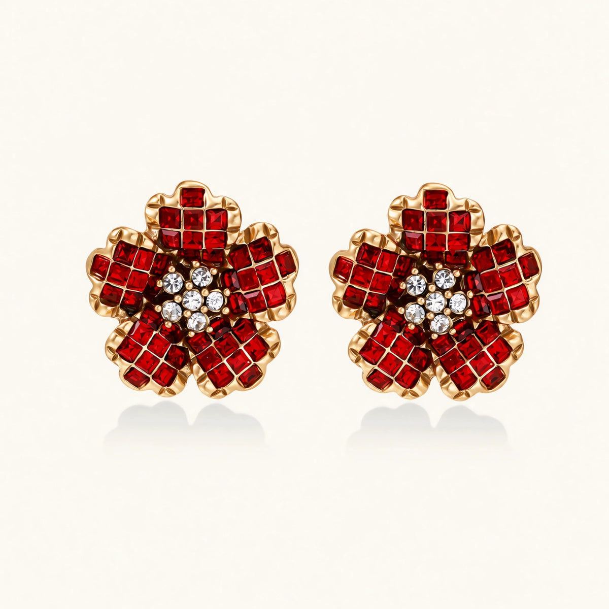 Gold-plated flower studs with burgundy square crystals in petal mosaic and clear center stones on beige background.