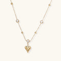 Delicate gold-plated necklace with bezel-set crystals and small heart pendant on beige background