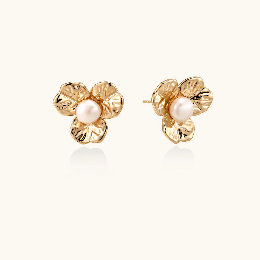 Gold-plated flower stud earrings with textured petals and centered freshwater pearl on beige background