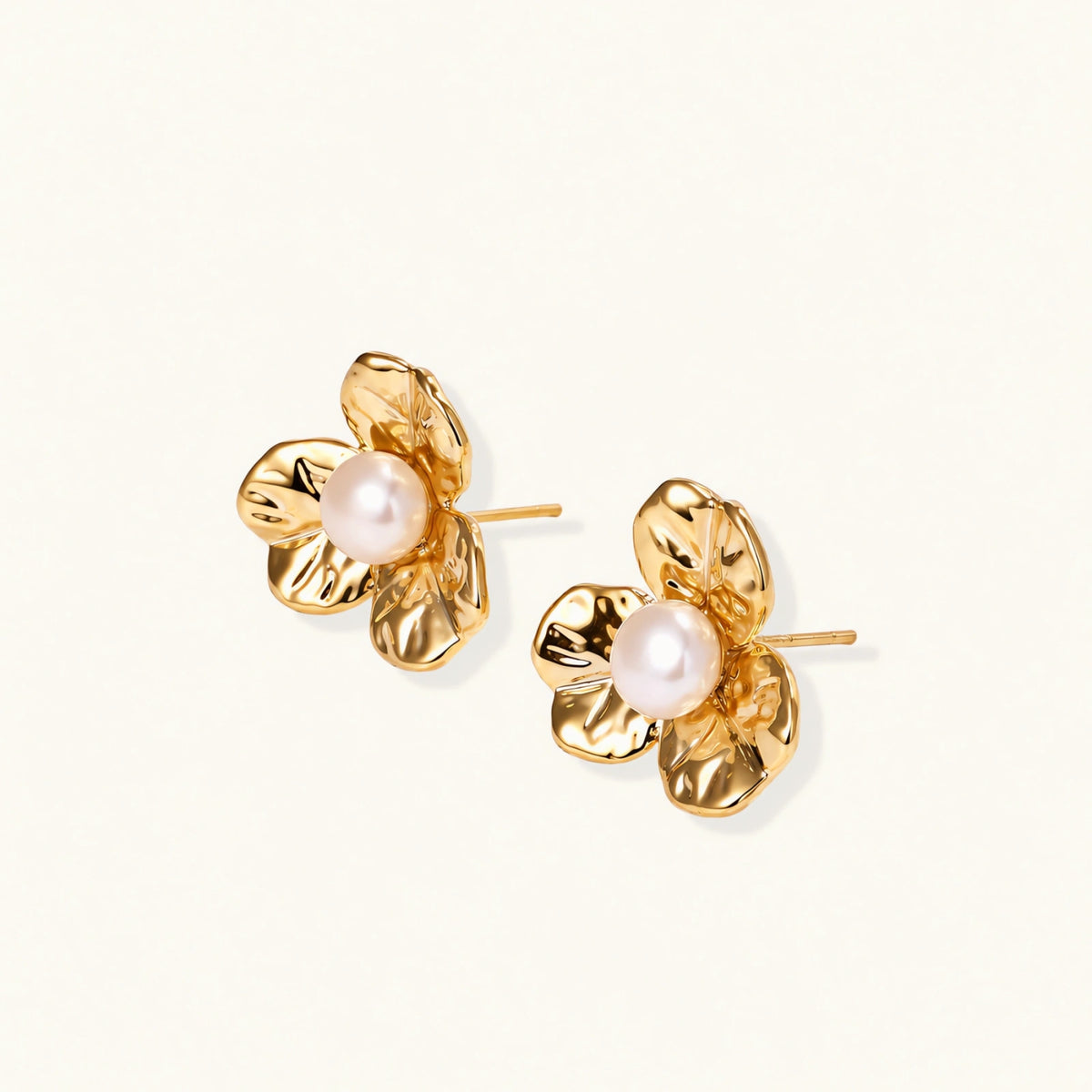 Gold-plated flower stud earrings with textured petals and centered freshwater pearl on beige background
