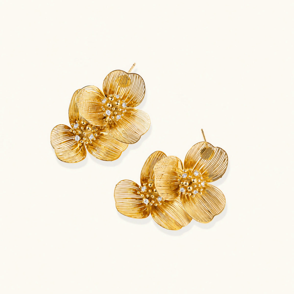 Pair of gold-plated double flower earrings with textured petals and crystal centers on cream background.