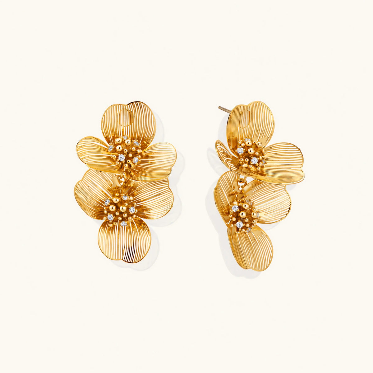 Pair of gold-plated double flower earrings with textured petals and crystal centers on cream background.