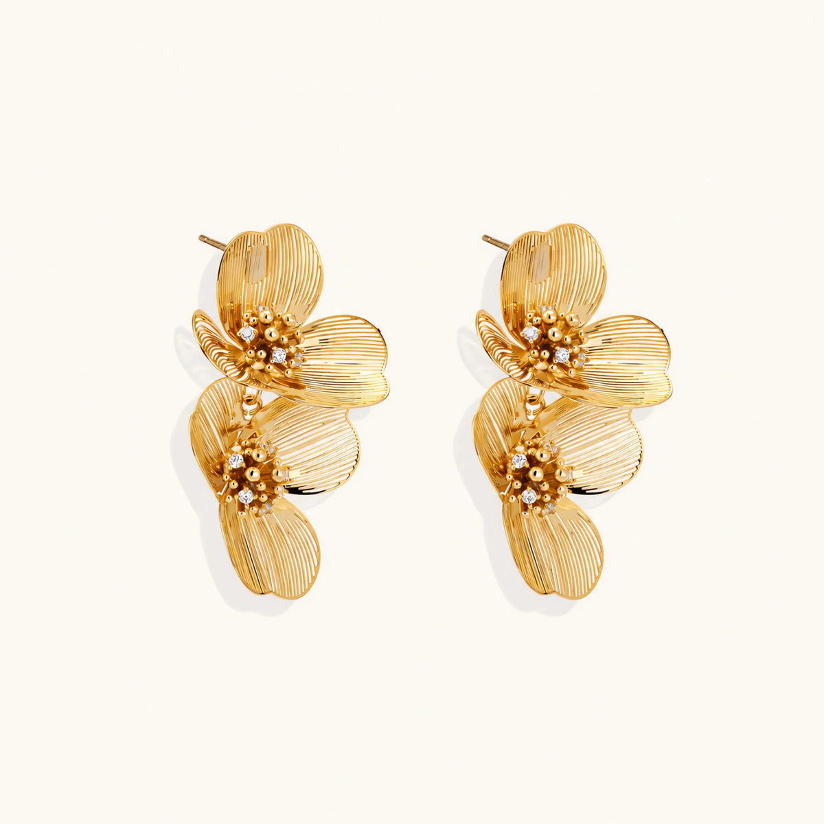 Pair of gold-plated double flower earrings with textured petals and crystal centers on cream background.