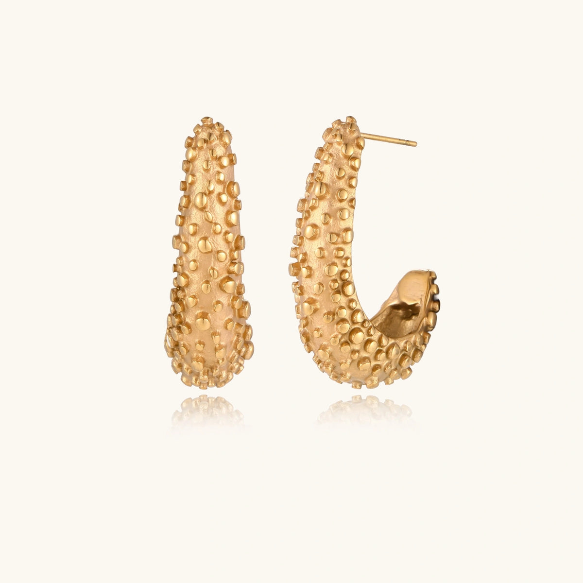 Curved gold hoop earrings with raised granulated texture resembling sea urchin surface on cream background