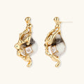 Gold-toned dangle earrings with marbled resin stones and flowing serpentine chain design on neutral background